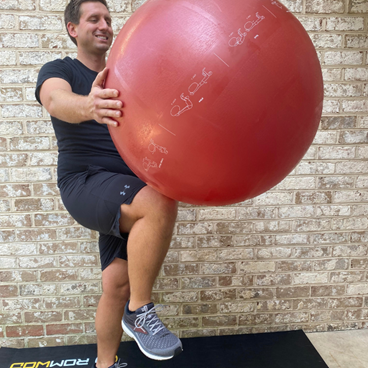 man standing exercise ball propped up on knee